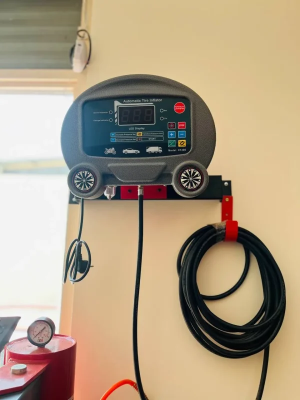 An automatic tire inflator mounted on a wall. The device features a digital LED display and several buttons for controlling tire inflation. It includes icons representing different types of vehicles, such as motorcycles, cars, and trucks. The model number "CT469" is visible on the device. Below the inflator, a coiled black hose with a pressure gauge is attached to a red cylinder. The buttons are labeled with functions such as "Increase Pressure," "Decrease Pressure," "Transform Pressure Unit," "Start," and "Stop."