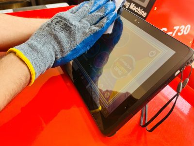 "A person wearing a blue and gray glove cleans a tablet screen with a cloth. The tablet rests on a red surface. In the background, there is a machine labeled 'Rebuilder Charging Machine' with the model number 'C-730.' Two chairs are also visible. The image includes Persian text that translates to 'Golden tips for maintaining diagnostics.