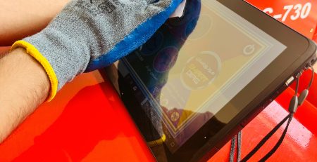"A person wearing a blue and gray glove cleans a tablet screen with a cloth. The tablet rests on a red surface. In the background, there is a machine labeled 'Rebuilder Charging Machine' with the model number 'C-730.' Two chairs are also visible. The image includes Persian text that translates to 'Golden tips for maintaining diagnostics.