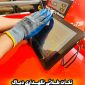 "A person wearing a blue and gray glove cleans a tablet screen with a cloth. The tablet rests on a red surface. In the background, there is a machine labeled 'Rebuilder Charging Machine' with the model number 'C-730.' Two chairs are also visible. The image includes Persian text that translates to 'Golden tips for maintaining diagnostics.