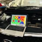 An open Kia vehicle hood with a laptop placed on the front grille. The laptop screen shows a colorful interface with various icons and Arabic text, likely related to vehicle diagnostics or maintenance